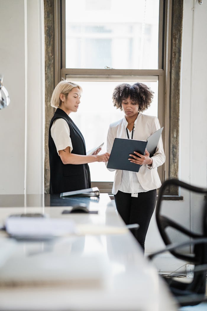 Two businesswomen discussing documents in a modern office setting.