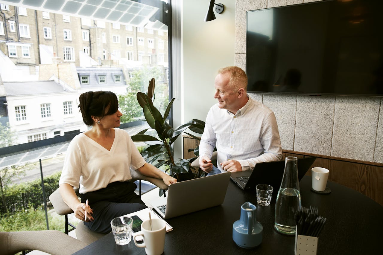 heros-img Two business professionals engaging in a team meeting in a modern London office with a large window view.